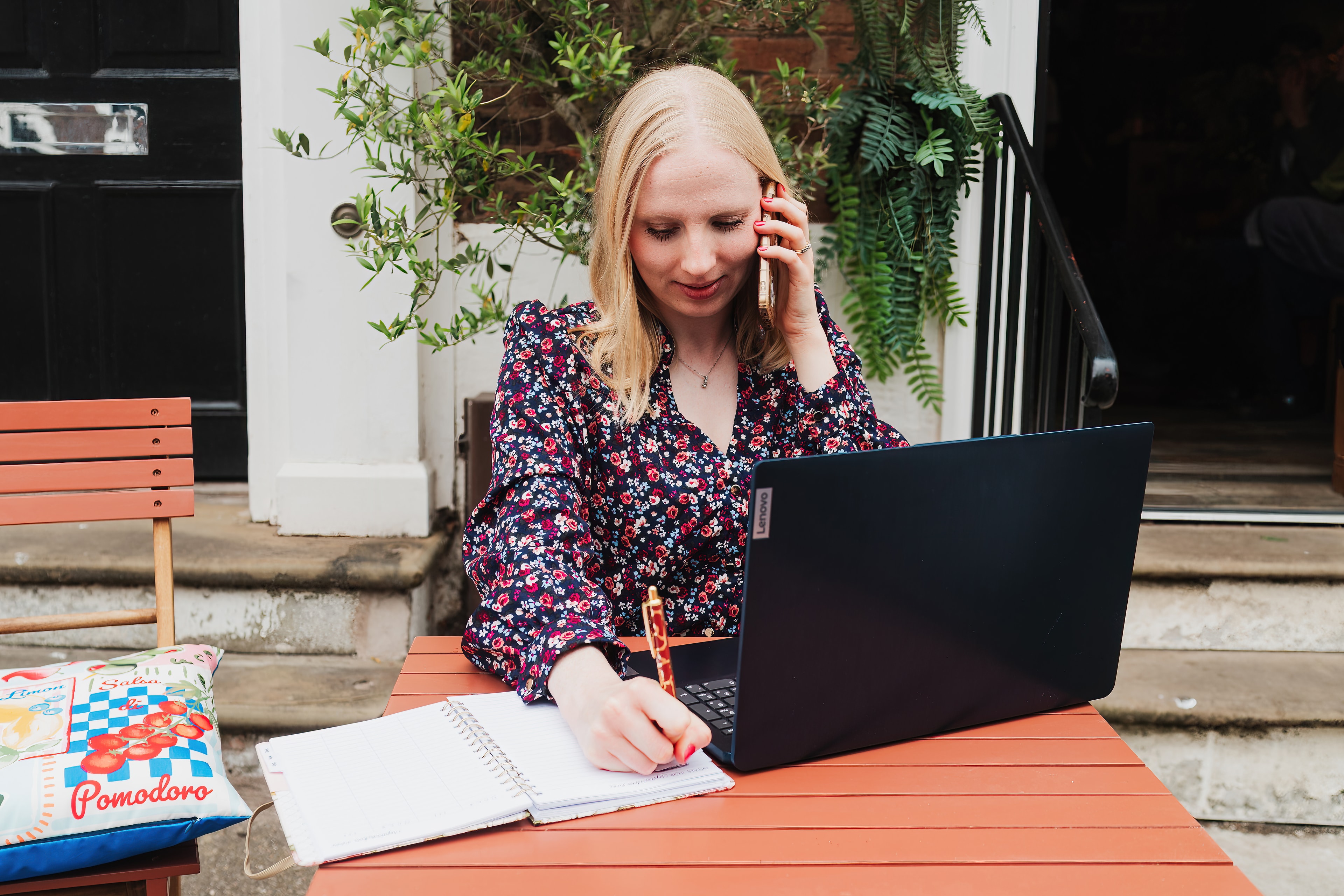 Hannah Pritchard working outdoors at a laptop, taking a call and making notes