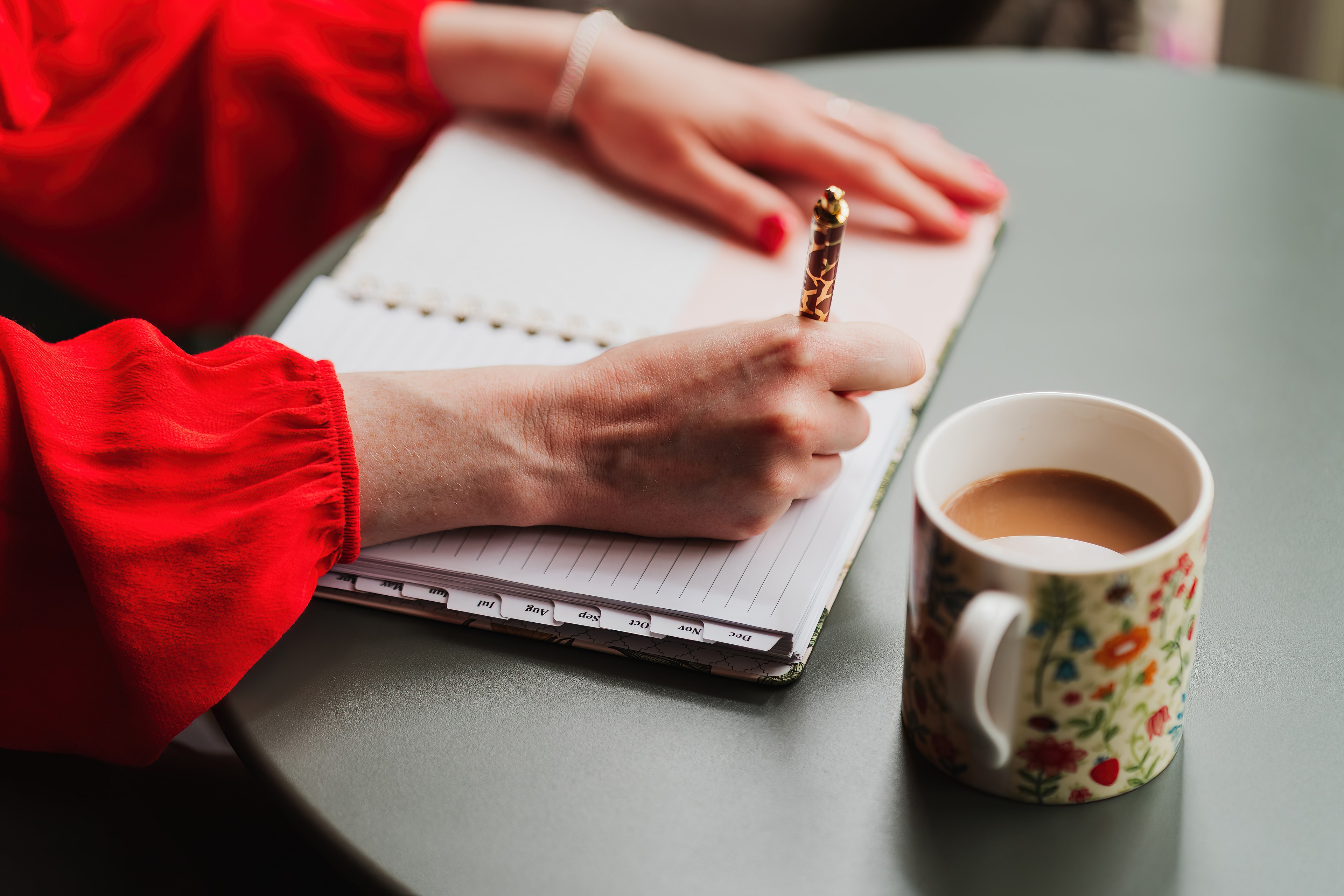 Close-up of Hannah writing in a notebook beside a floral mug of coffee